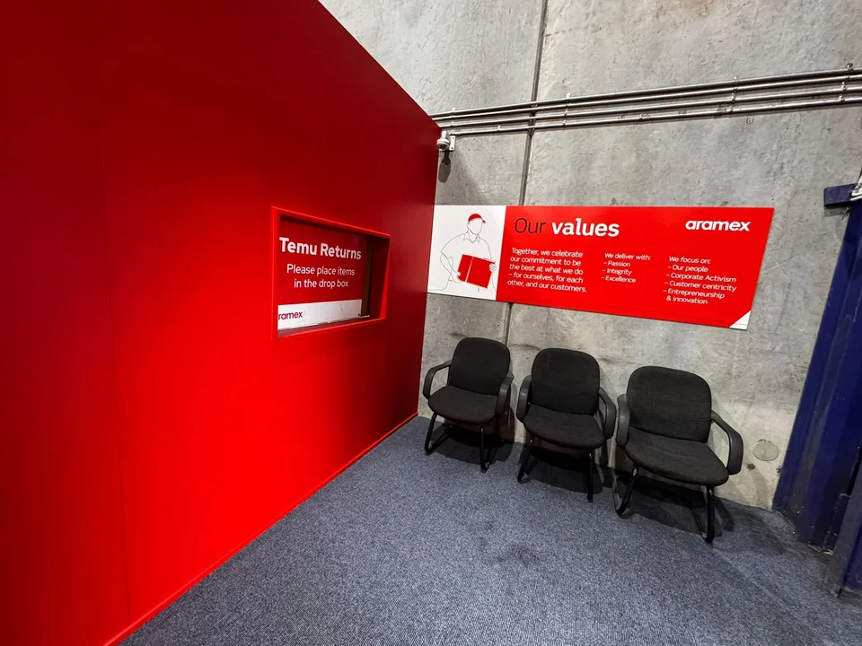 Red-walled Aramex corner with a Temu returns drop box and three chairs