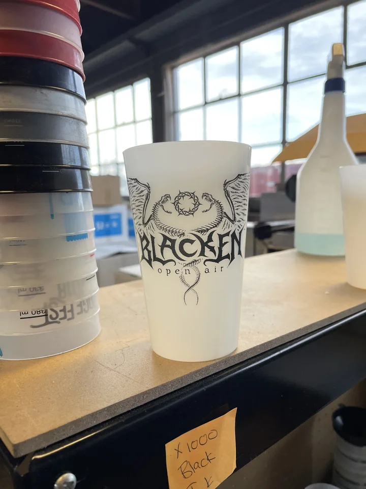 Cup printed with the Blacken logo beside a stack of cups
