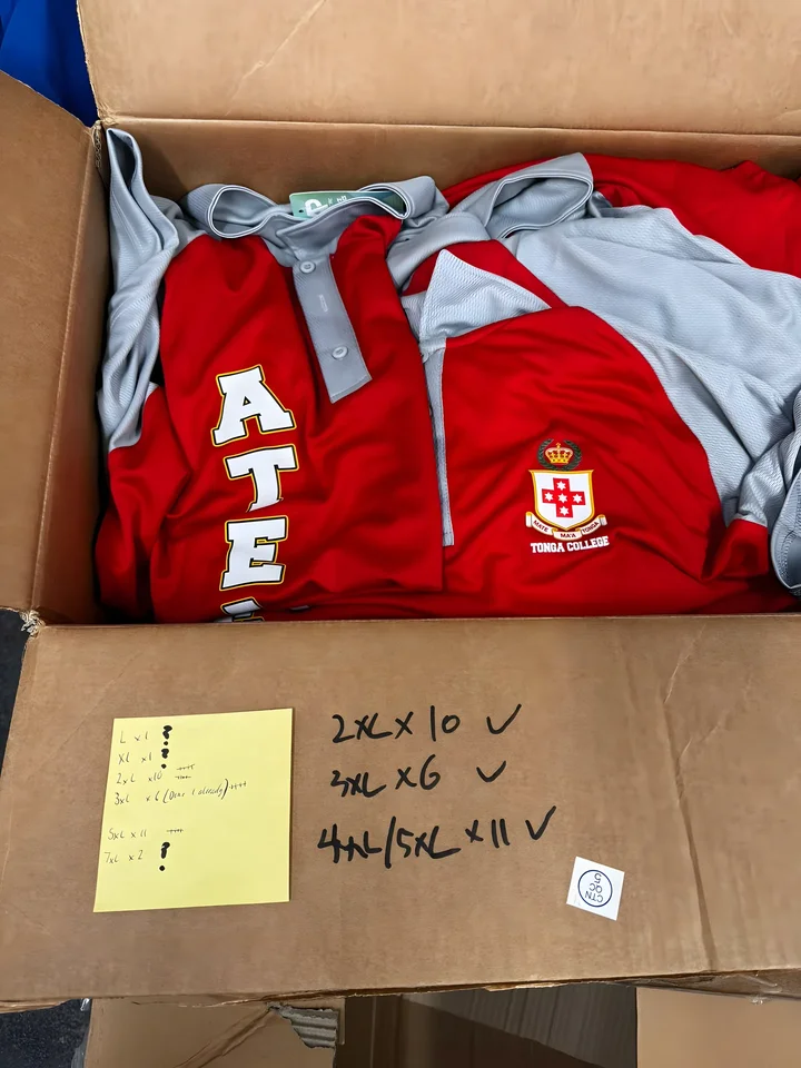 Box of finished red and grey polos with the order count on a sticky note